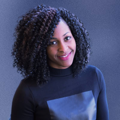 A woman with curly hair sitting in a chair, looking relaxed and content.